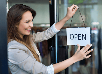 Young woman switches sign to open on door to small business
