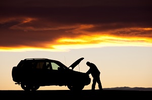 man looking in hood of car at sunset